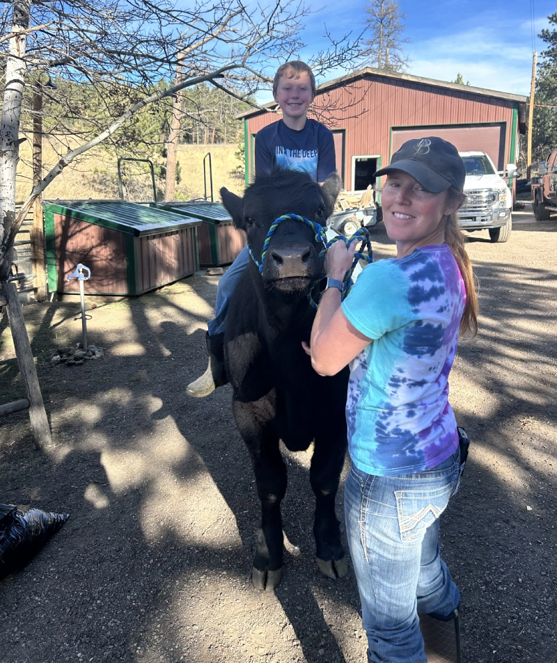 Woman and boy posing outdoors with a halter-trained black cow
